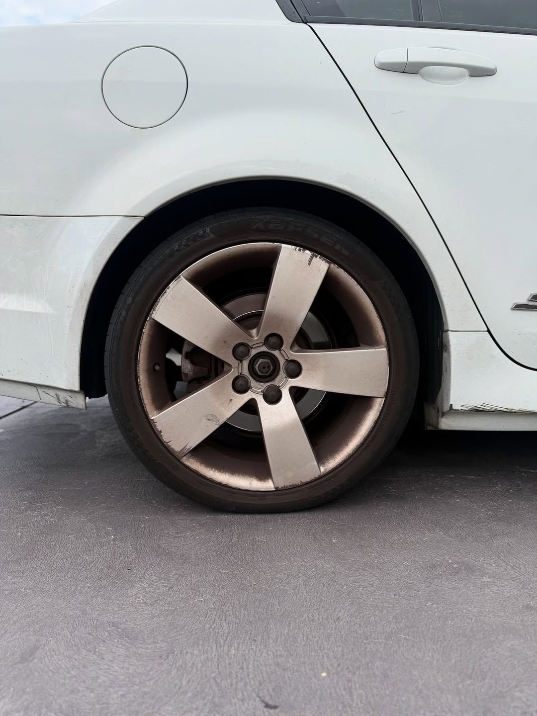 White car with a dirty silver rim. Rear tire visible.