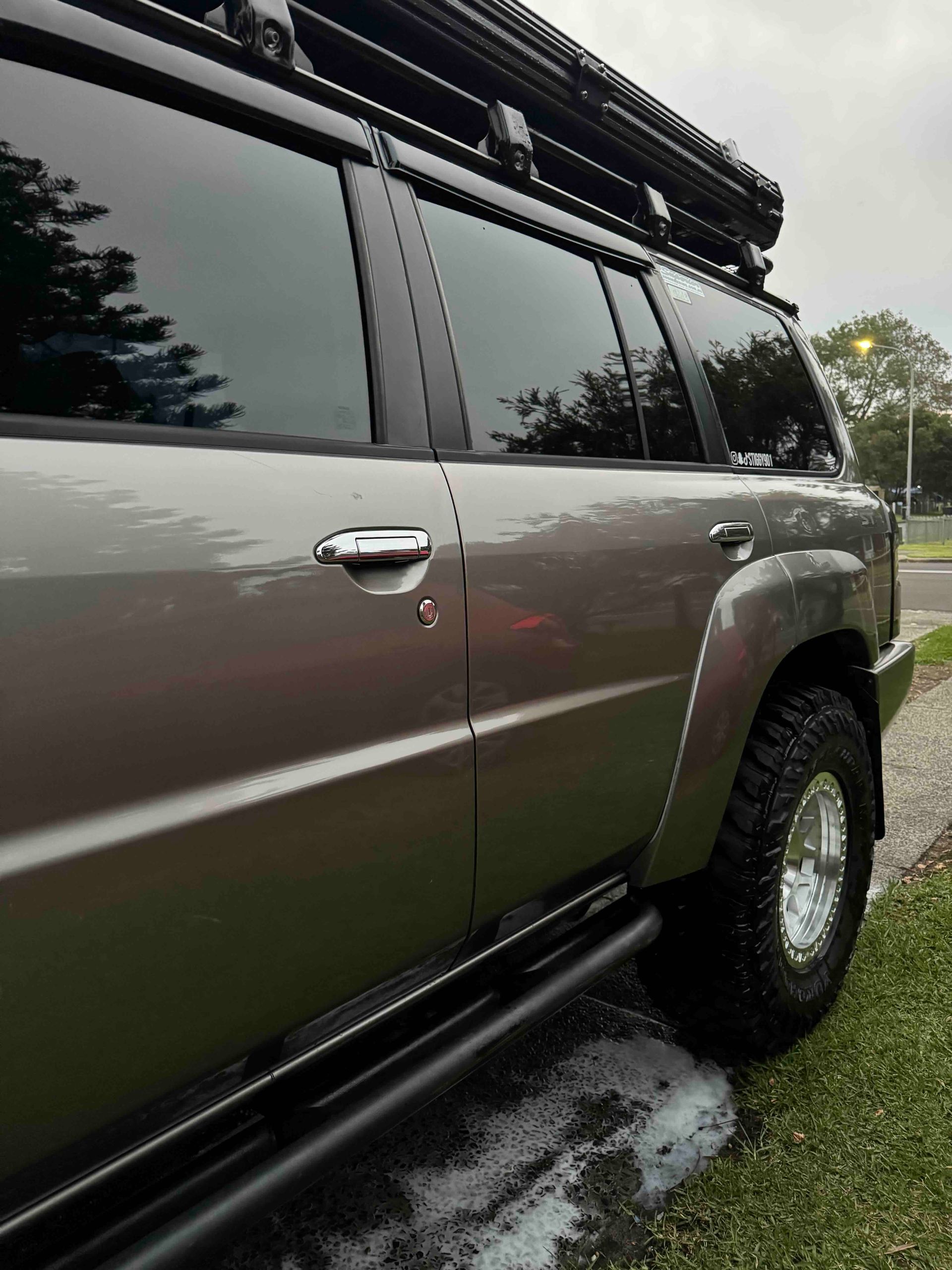 Gray SUV with tinted windows and off-road tires, parked on grass, with a roof rack.