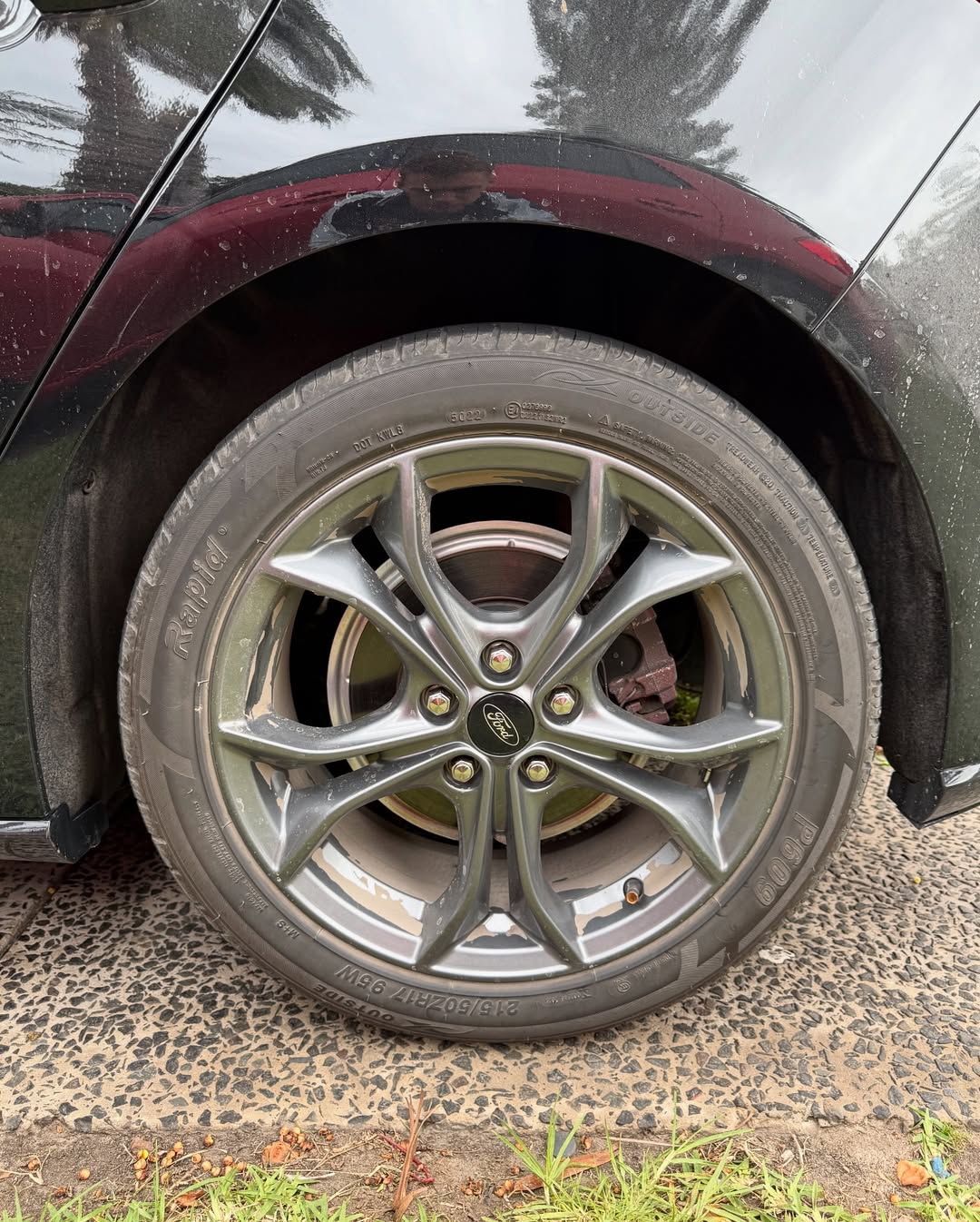 Close-up of a dark gray car wheel with a Ford emblem on a black car on a damp street.