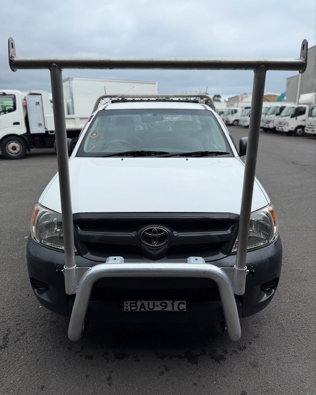 White Toyota Hilux truck with a silver bull bar and overhead rack, parked outdoors.