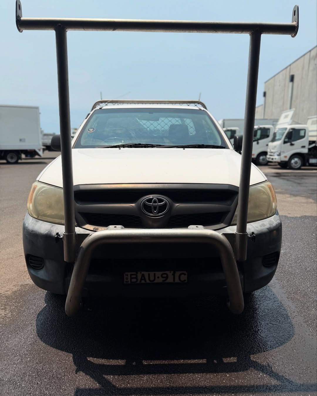 White Toyota Hilux pickup truck with metal bull bar and roof rack, parked outdoors.