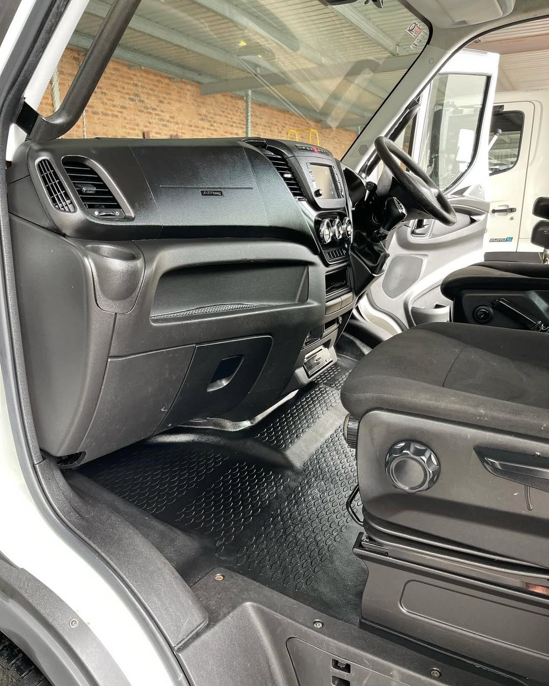 Interior view of a white van, showcasing the dashboard, driver's seat, and black rubber flooring.