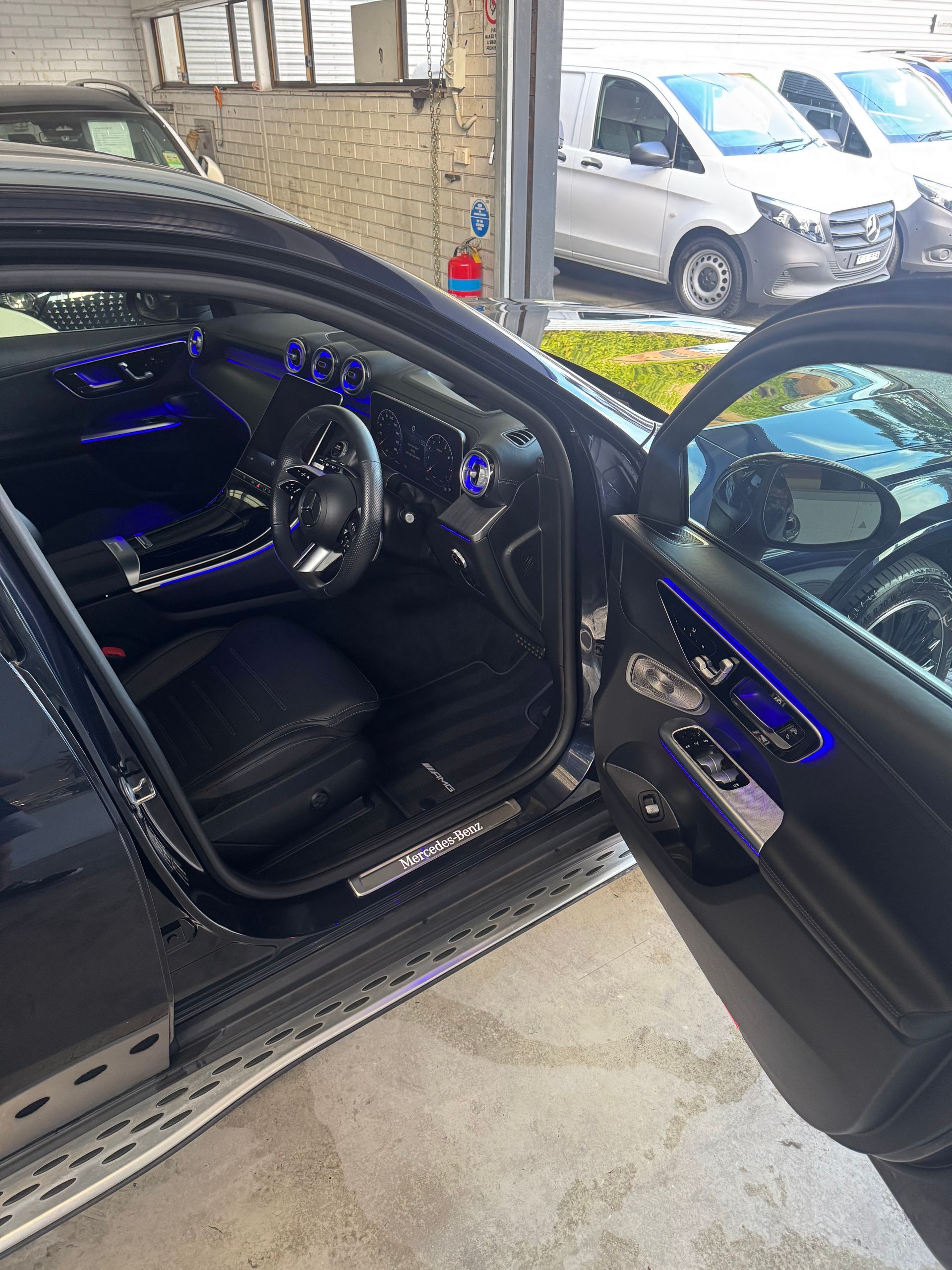 Black car interior with blue ambient lighting, open door, parked outdoors.