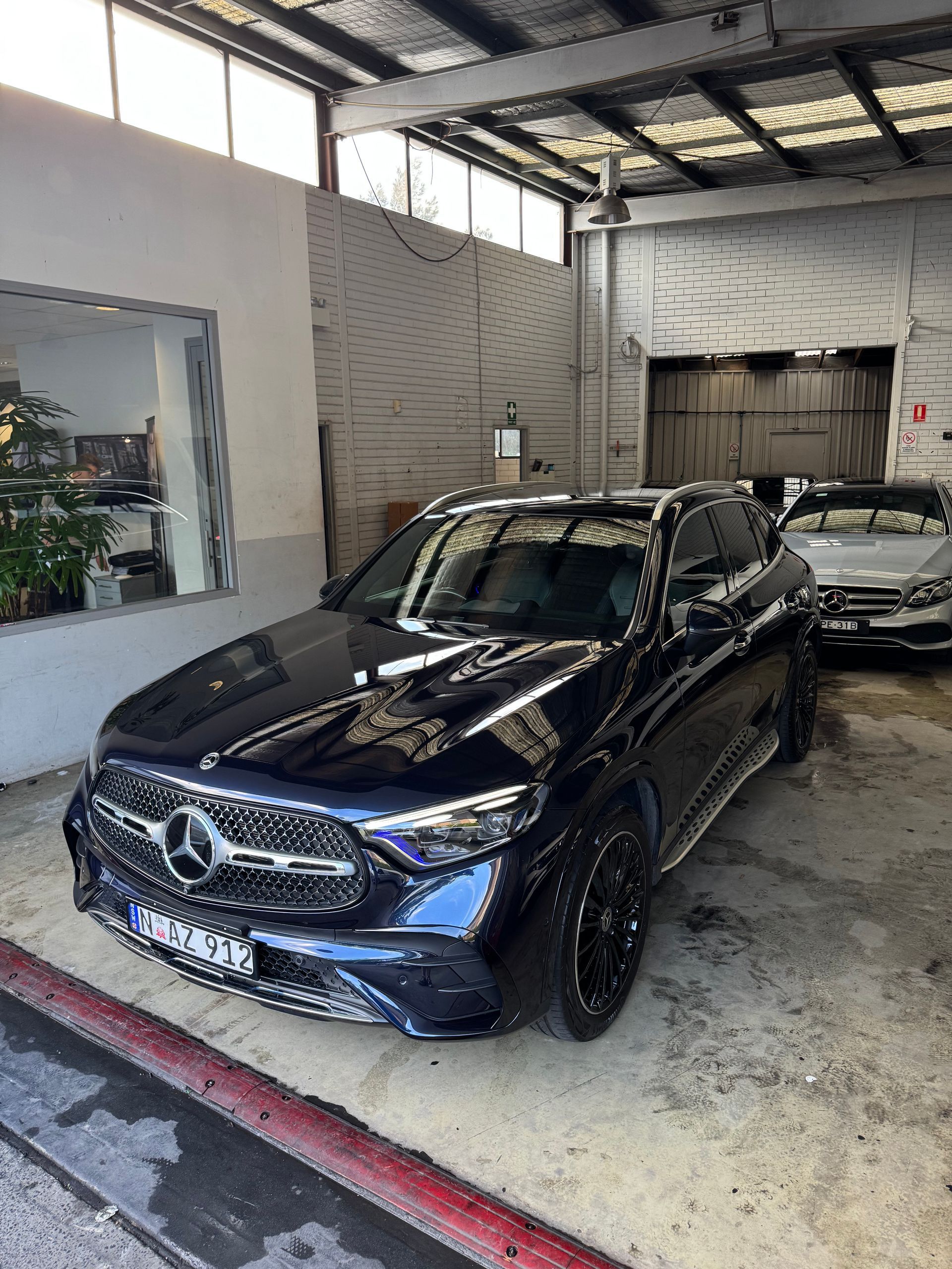 Dark blue Mercedes SUV parked inside a garage, near a window and other cars.
