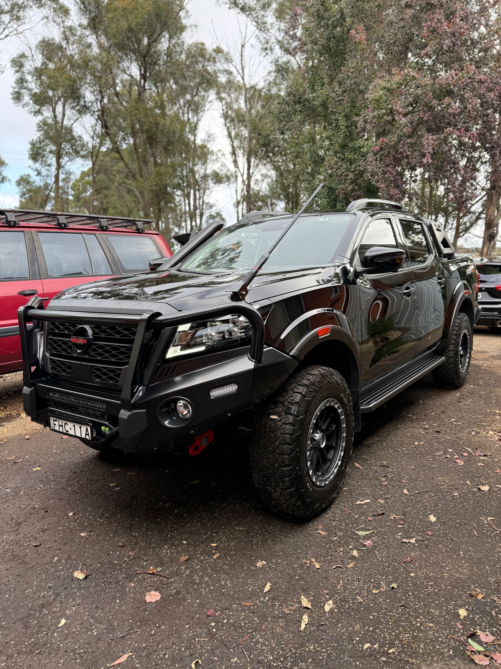 Black modified pickup truck with off-road features, parked on a dirt surface in a wooded area.