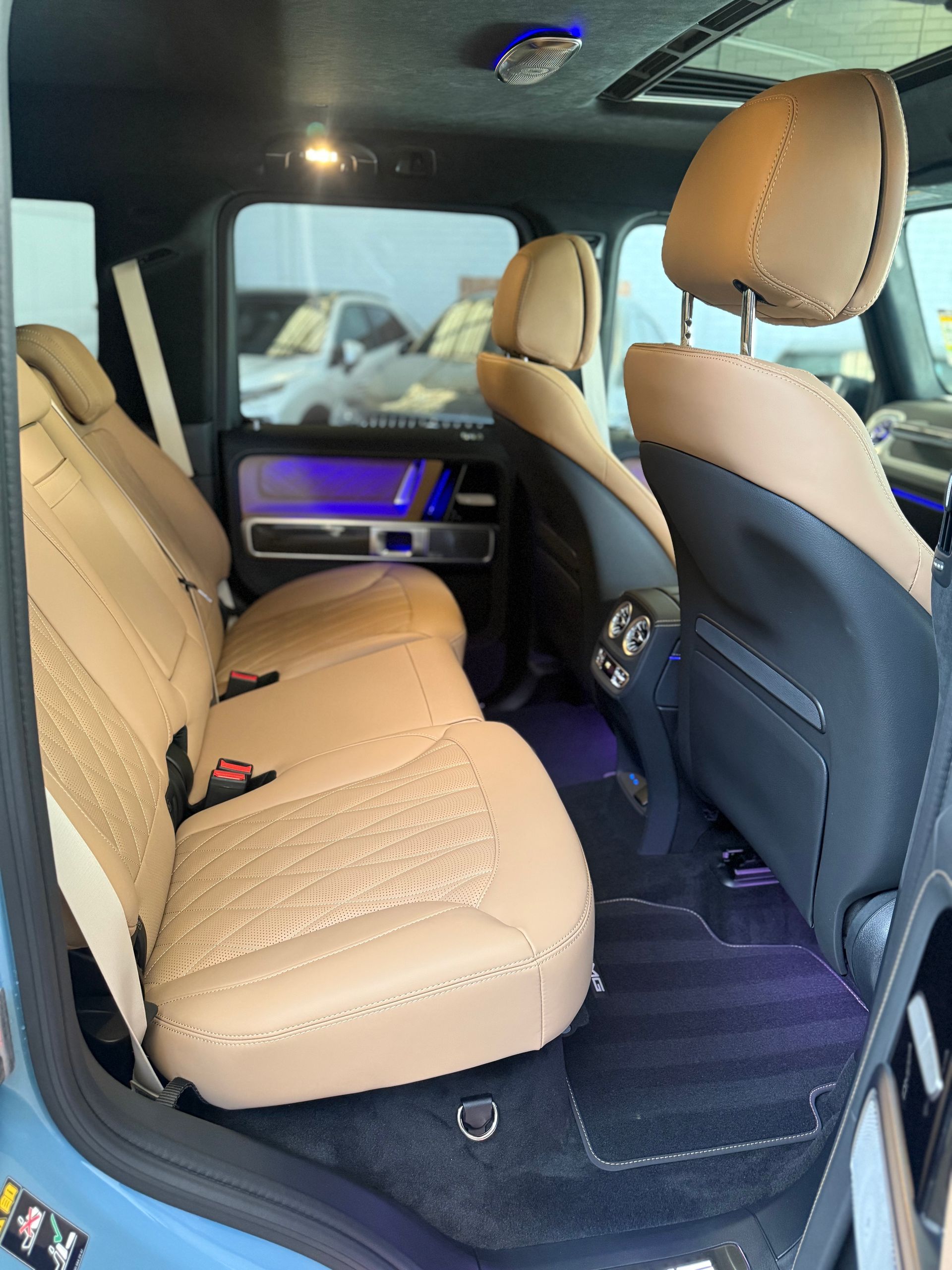 Interior view of a light brown leather car backseat with black carpet.