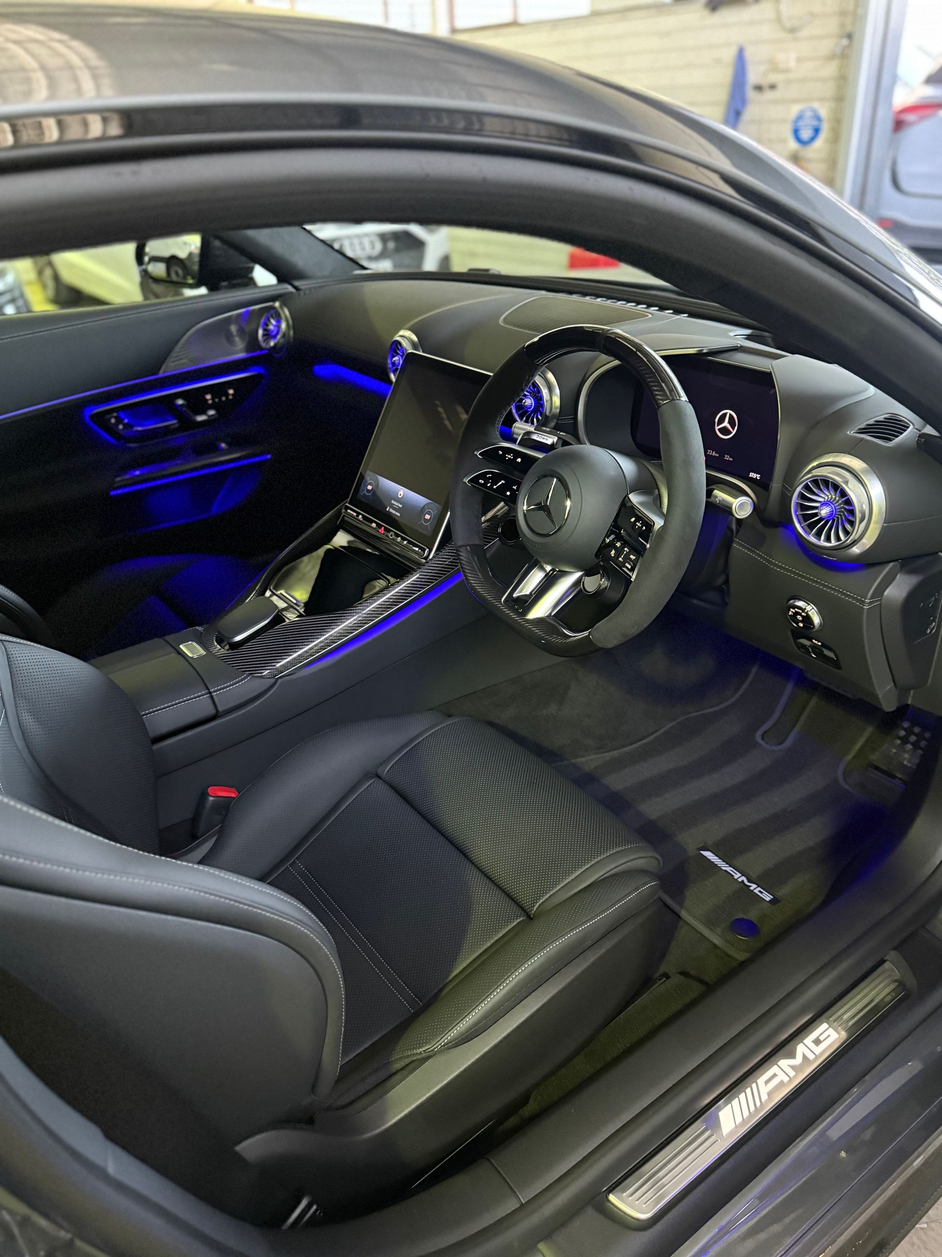Black Mercedes-AMG GT interior with blue ambient lighting, black leather seats, steering wheel, and console.