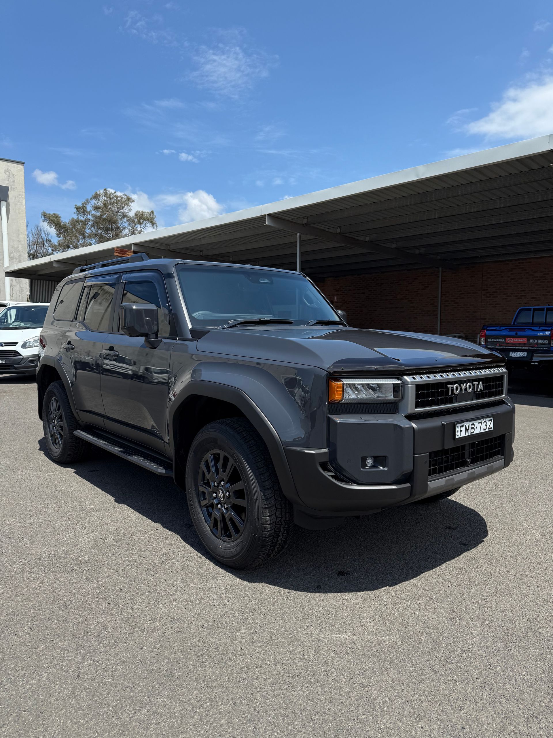 Dark gray Toyota SUV parked on gravel under a blue sky.