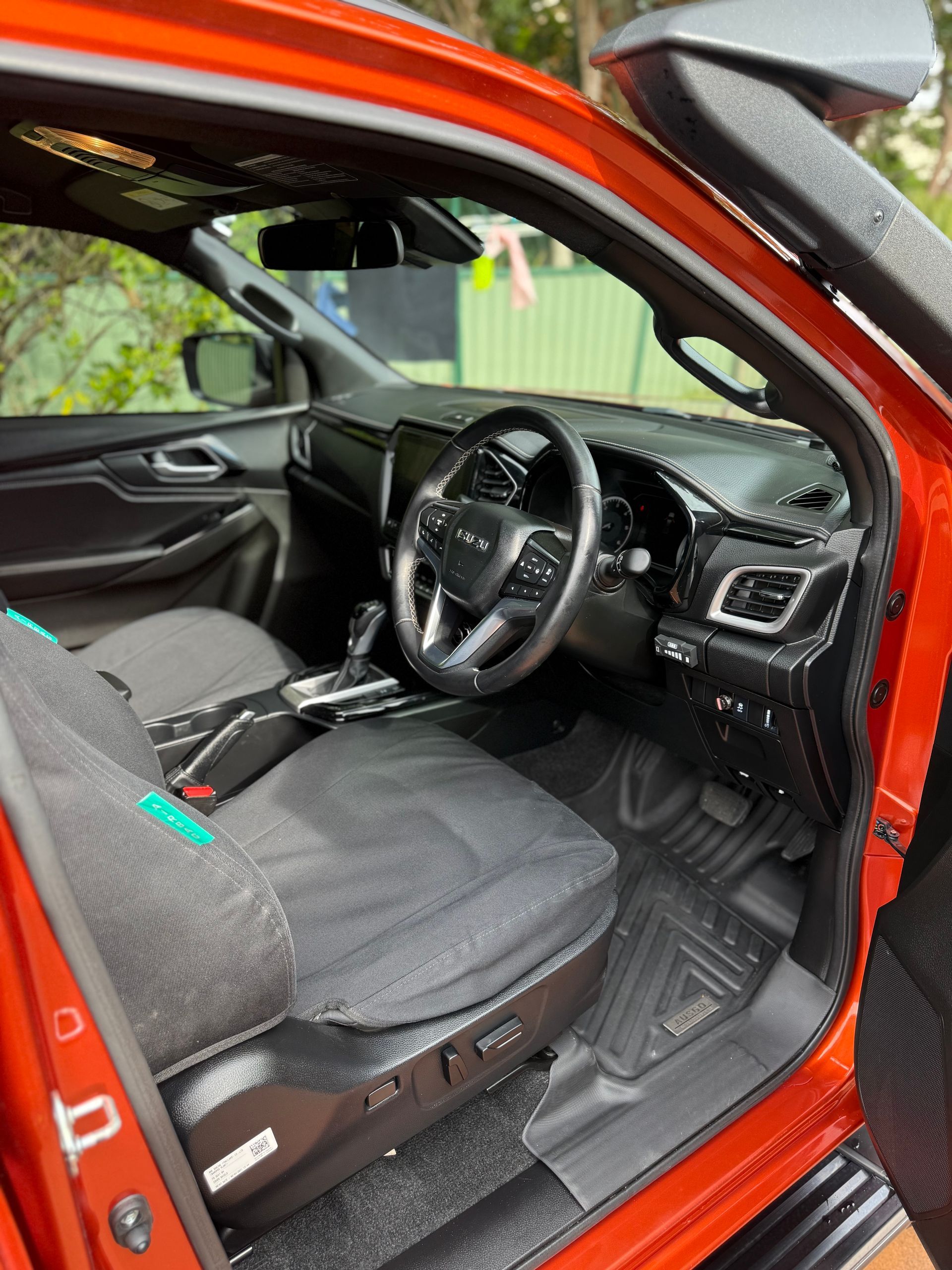 Orange car interior, driver's seat visible. Black seat cover, steering wheel, dashboard, and open door.