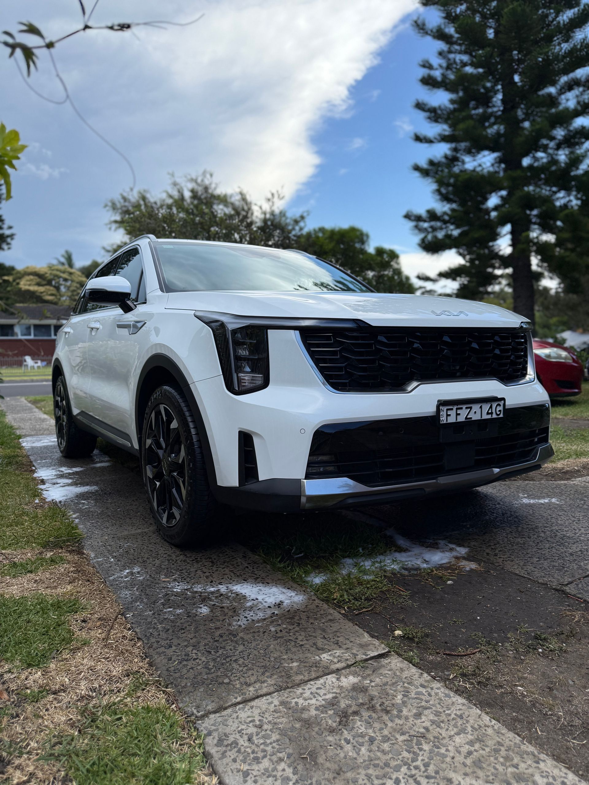 White SUV parked on a driveway with black grille and wheels. Blue sky.
