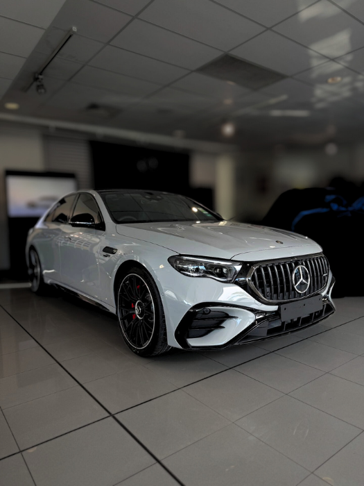 White Mercedes-AMG electric sedan in a showroom, black wheels, and a black grille with the Mercedes star emblem.
