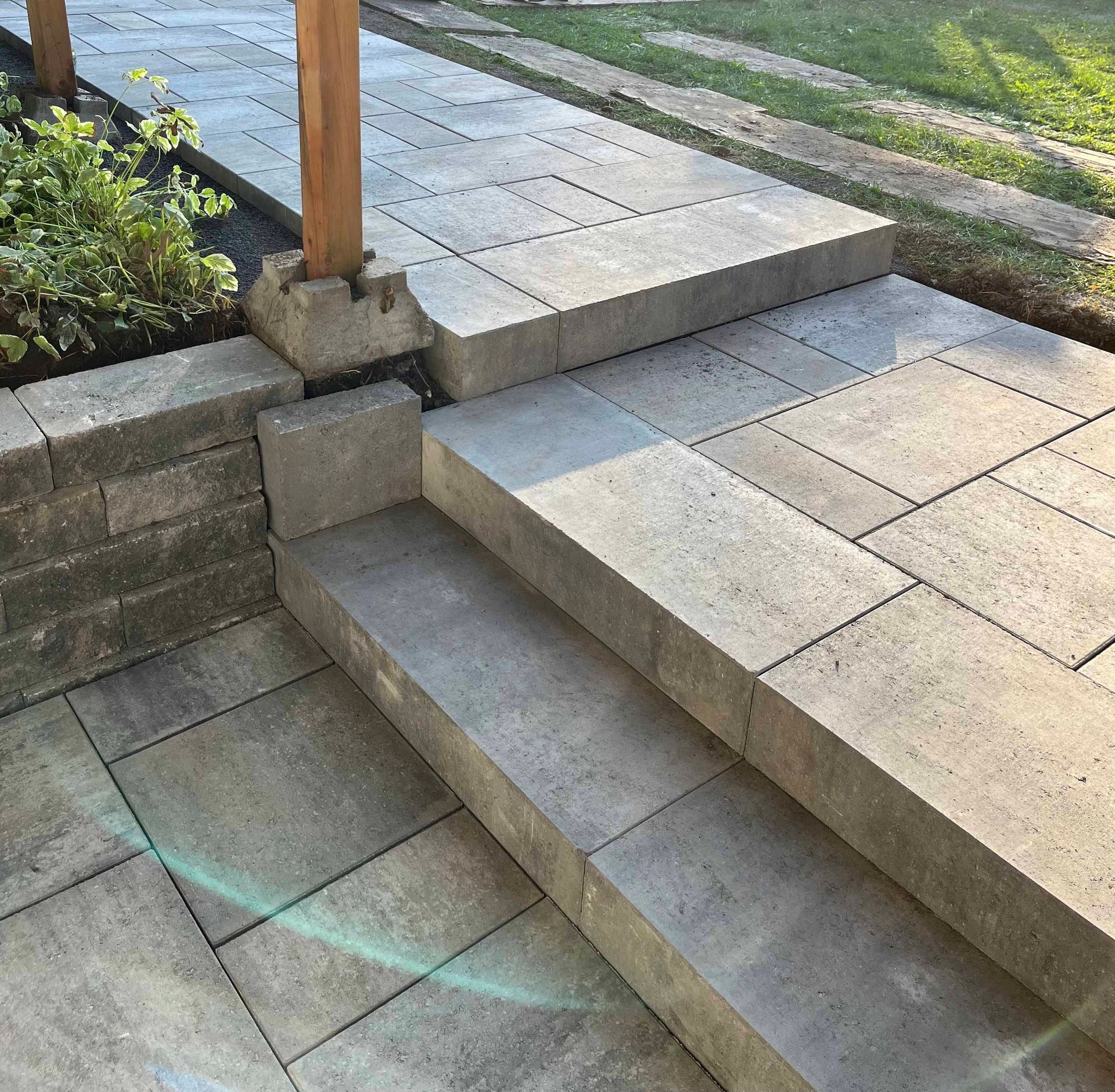 Un escalier en pierre mène à une terrasse surélevée, adjacente à un muret et à un poteau en bois.