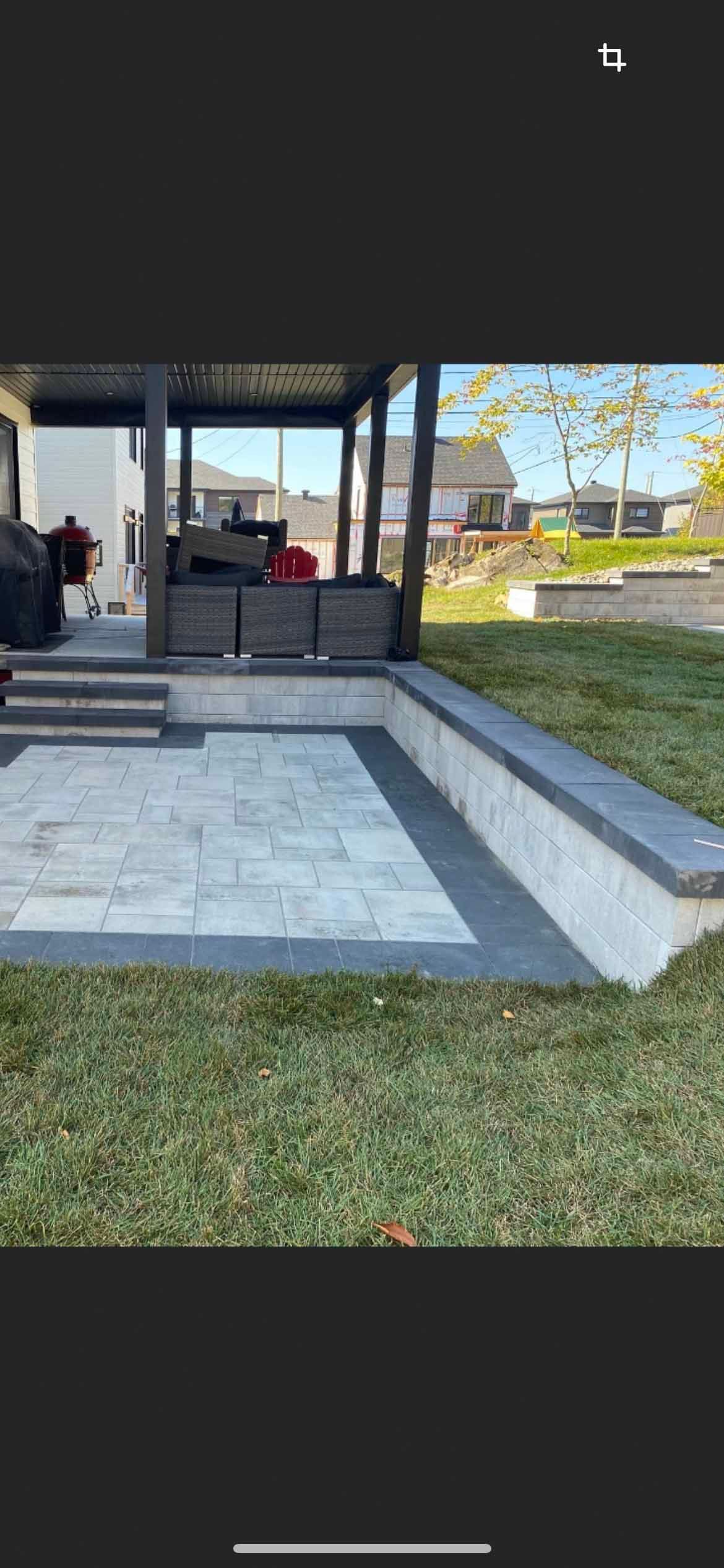 Une terrasse arrière avec des dalles de pierre claire, des bordures en pierre foncée, un mur de soutènement et un coin salon couvert.