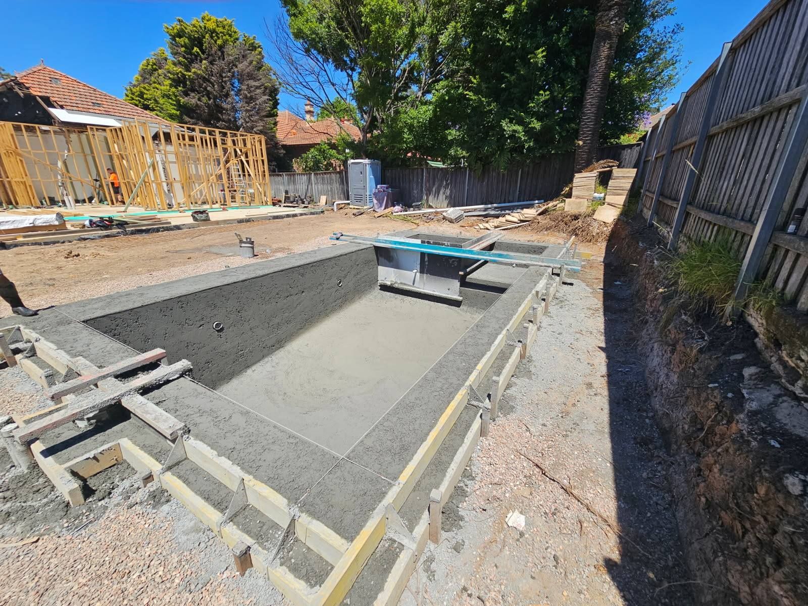 Backyard with an unfinished rectangular pool excavation and concrete walls under construction