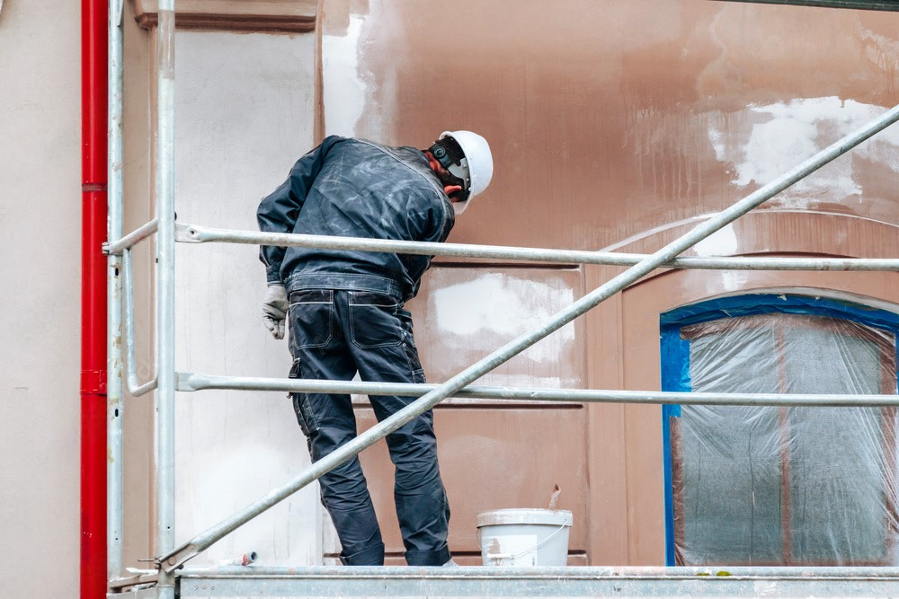 a man is standing on a scaffolding painting a building .