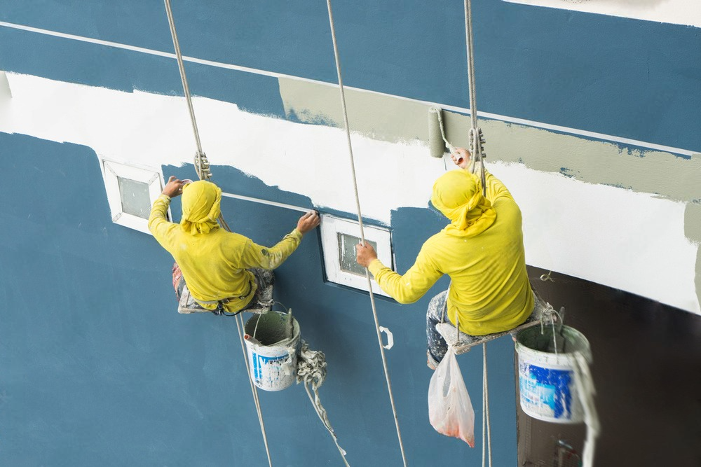 two men are painting a wall with buckets of paint hanging from ropes .