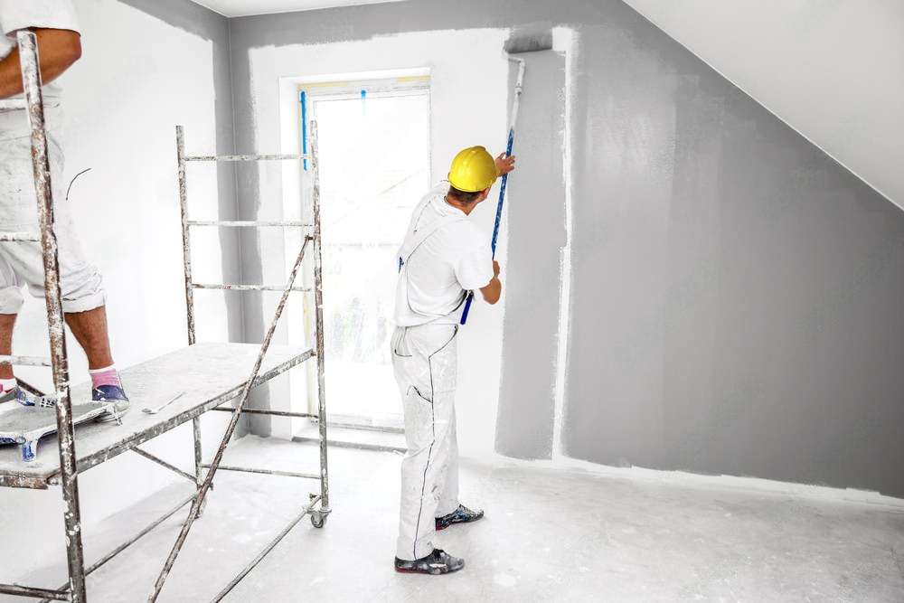 a man is painting a wall with a roller in a room .