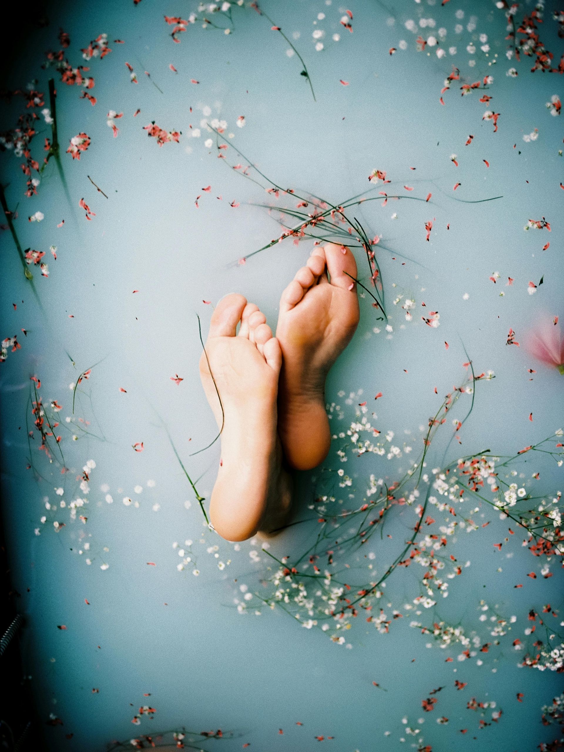 Feet in a light blue bath surrounded by flowers, soft lighting.