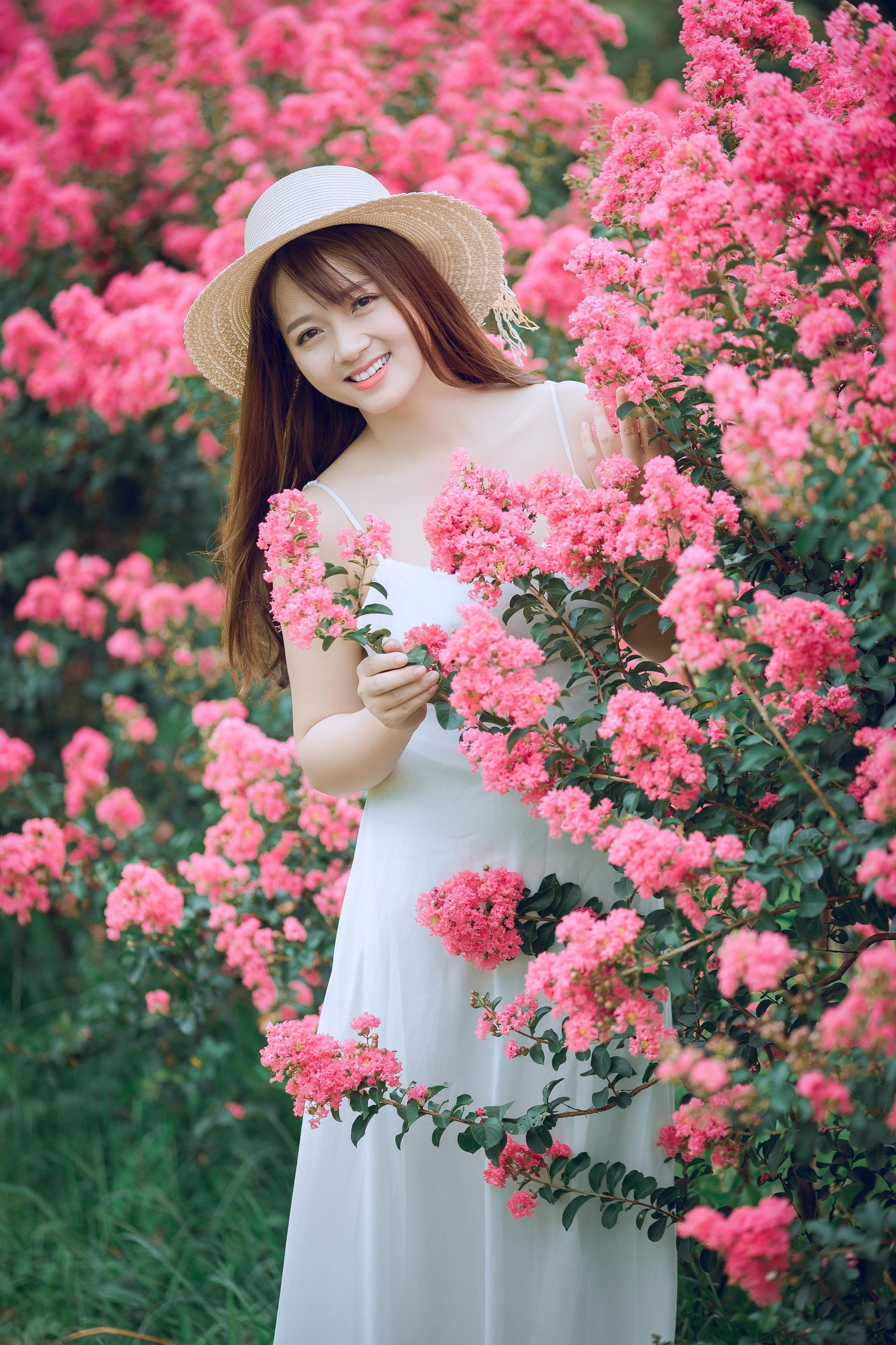 A woman in a white dress and hat is standing in a field of pink flowers.