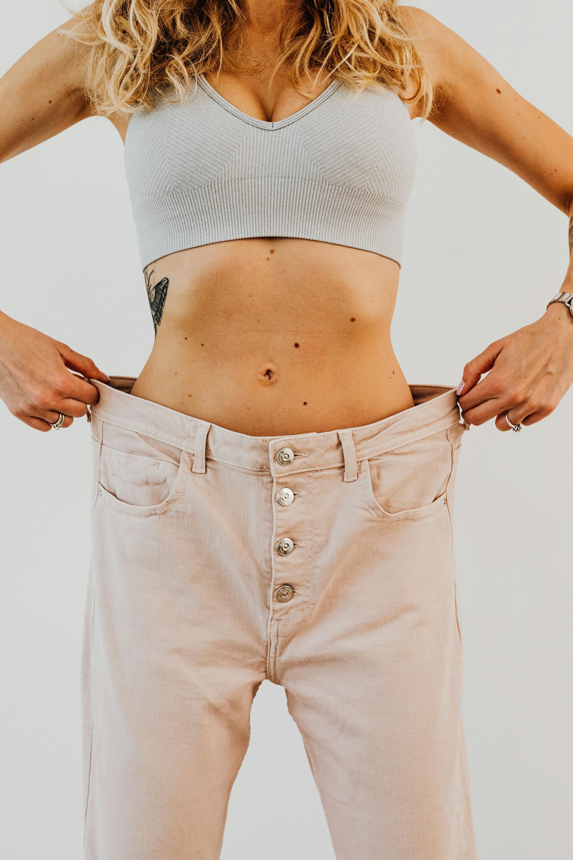Woman in a sports bra and oversized pants holding the waist, demonstrating weight loss.