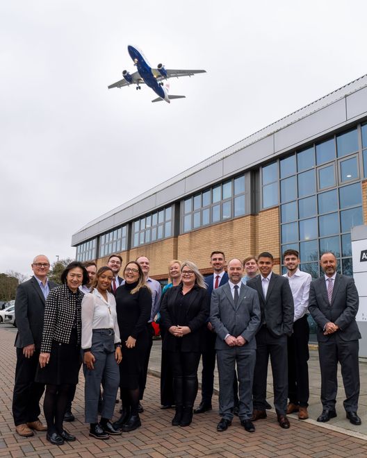 A group of people standing in front of a building with a plane flying overhead