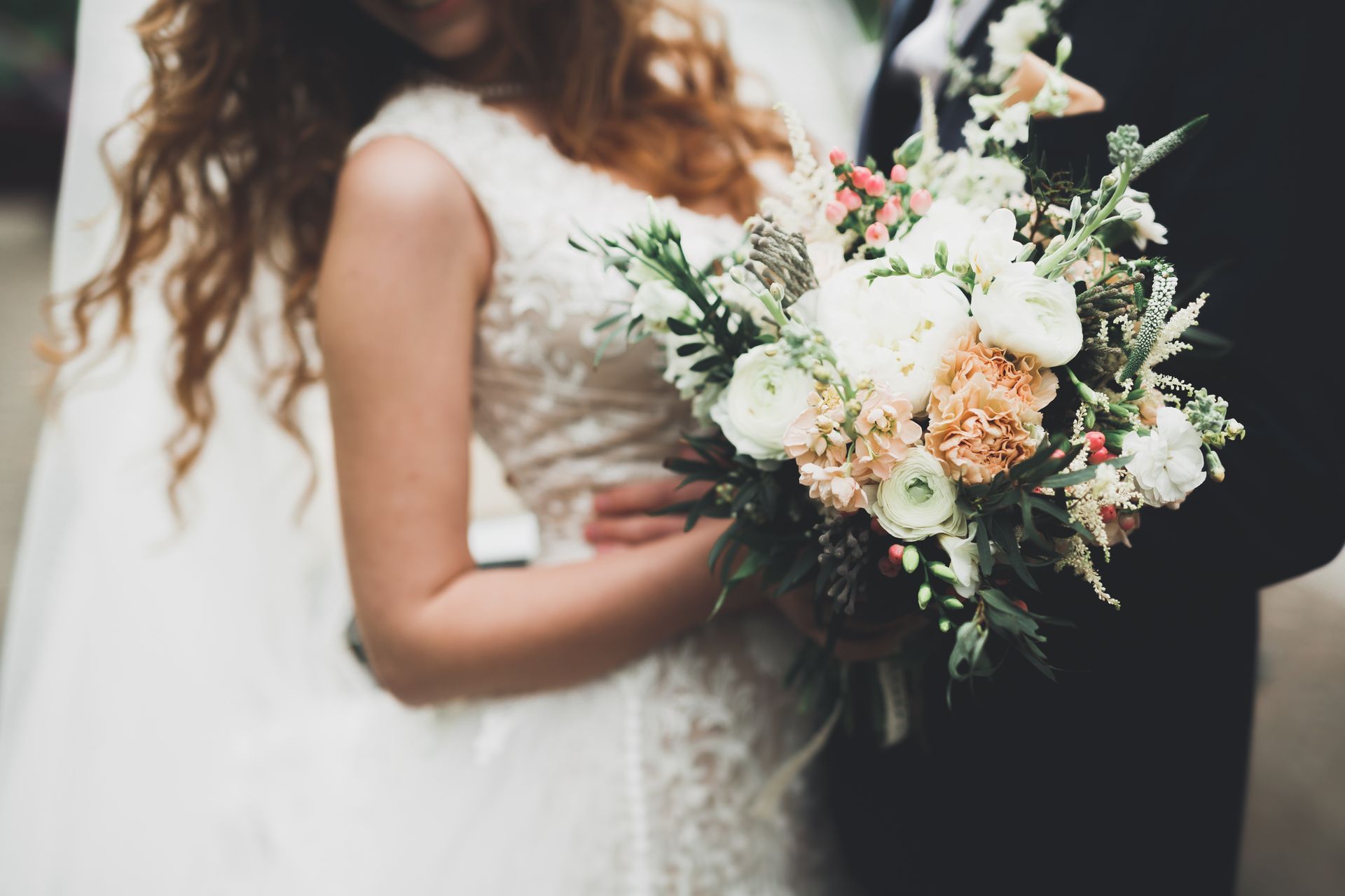 Bride holding a bouquet, embraced by the groom. Flowers include white and peach roses with greenery.