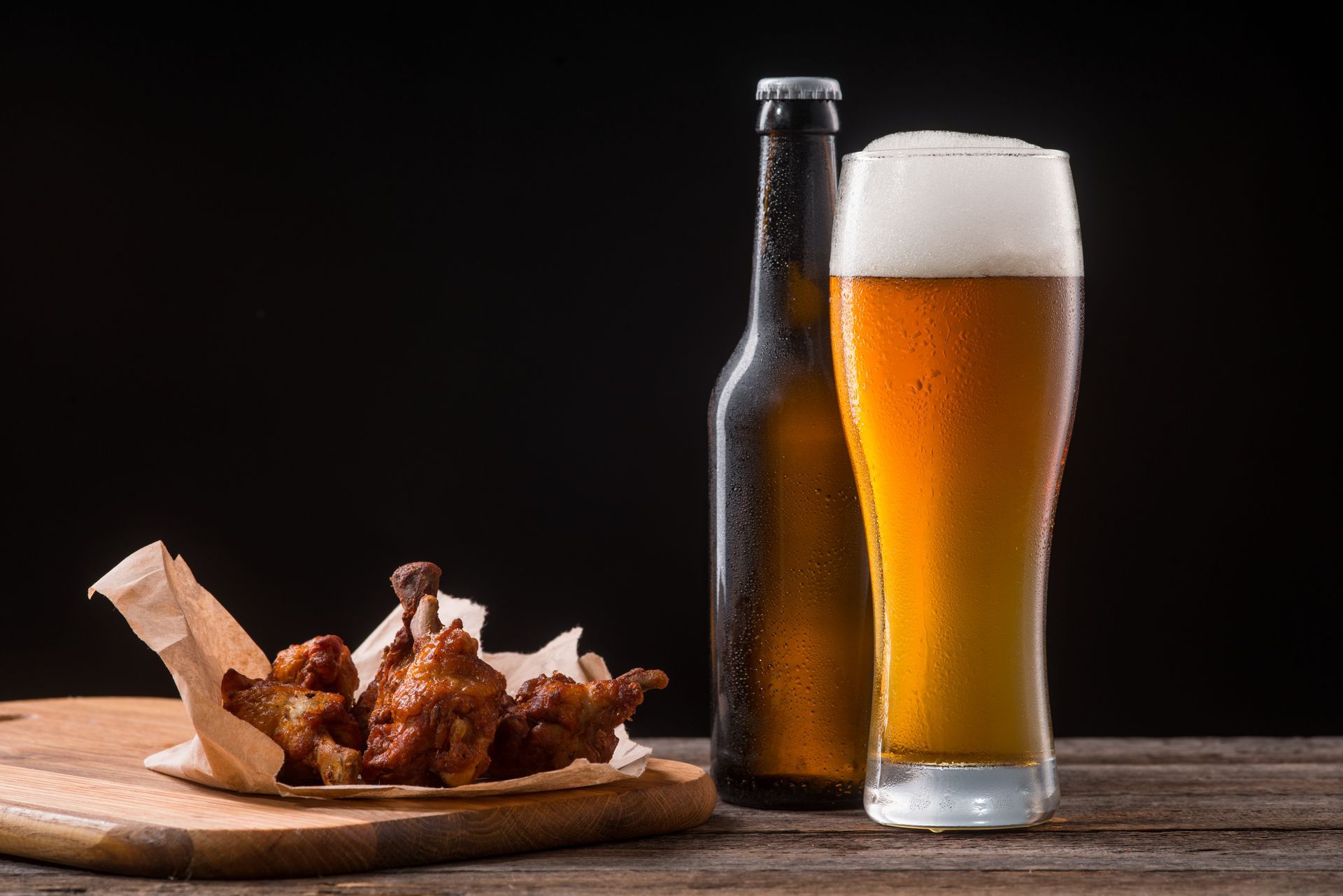 Chicken wings, beer bottle and pint of beer on a wooden table. Dark background.