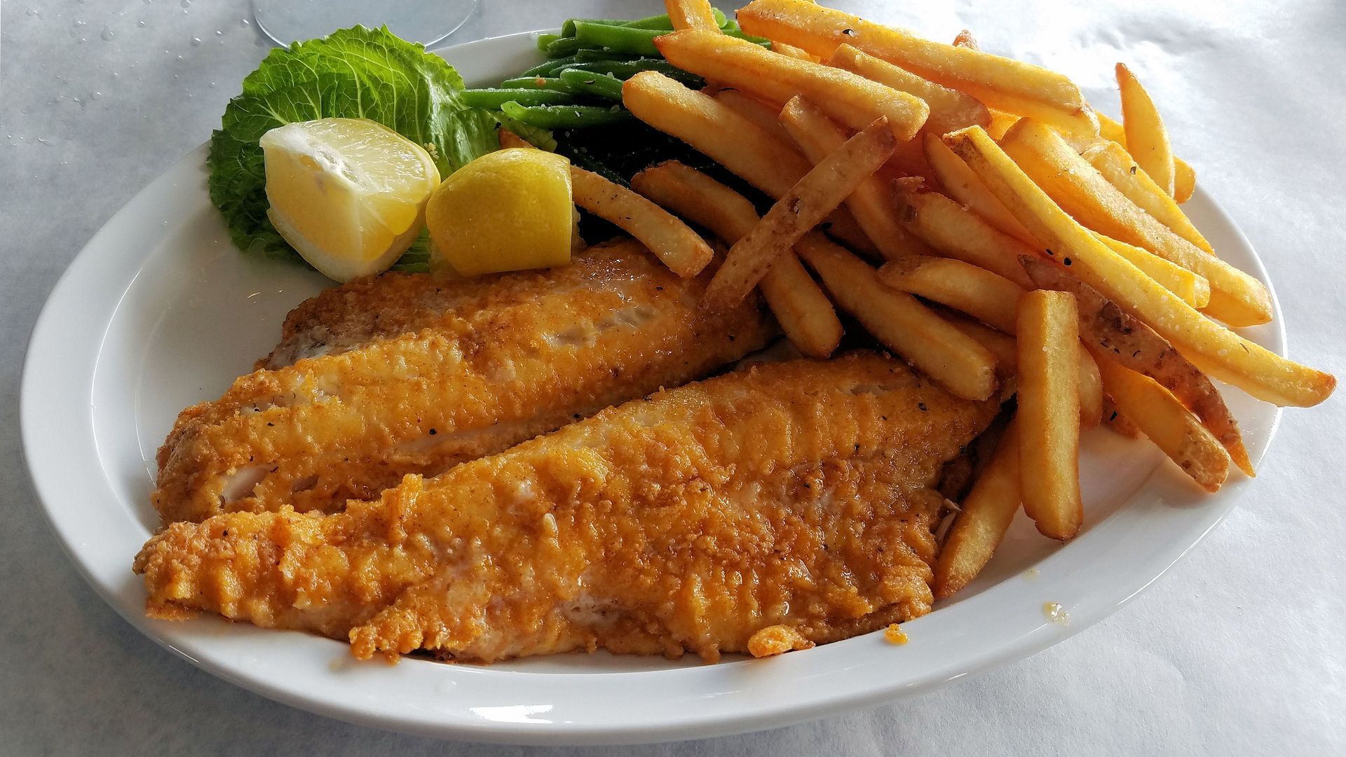 Fried fish fillets with fries, green beans, lemon, and lettuce on a white plate.