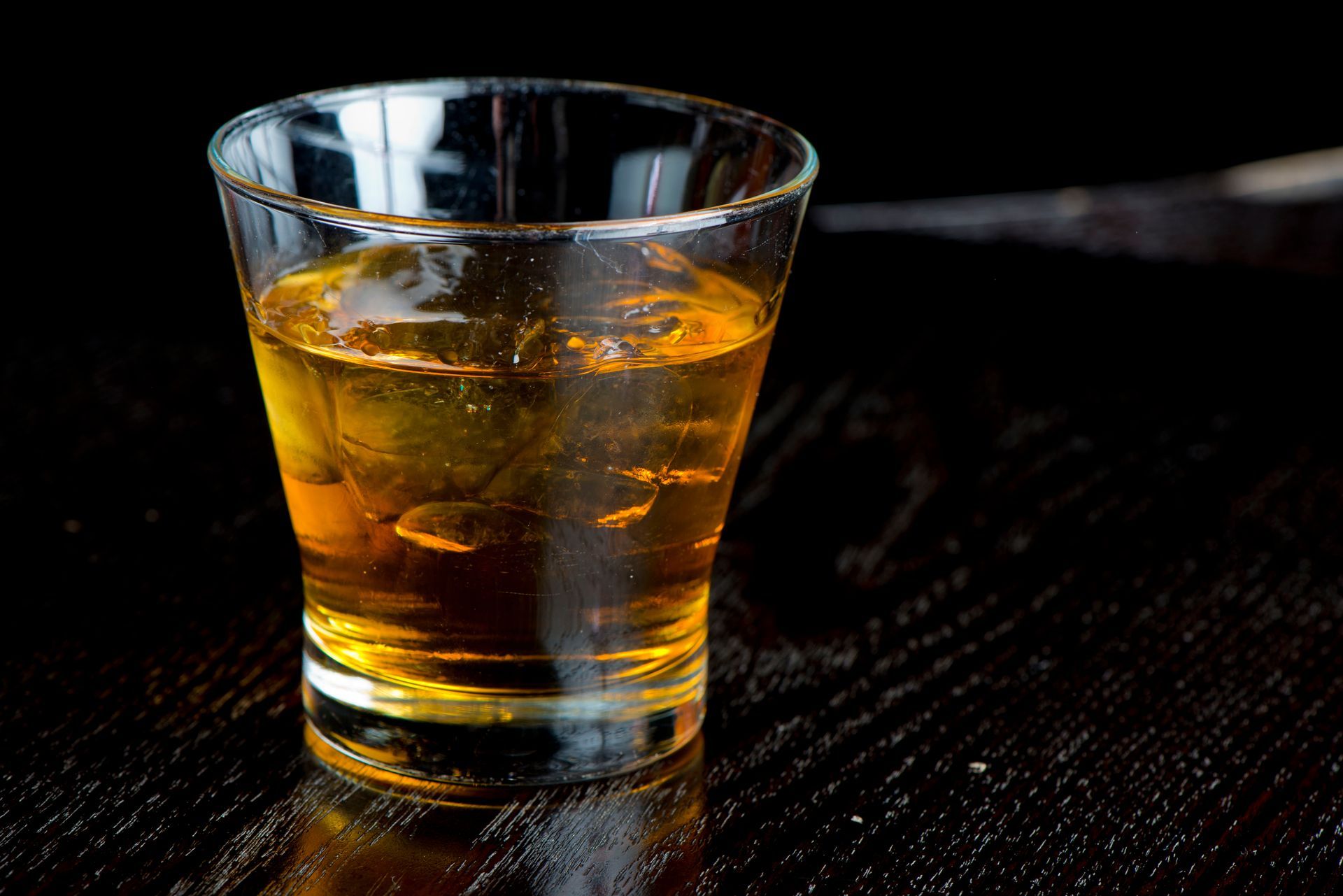 Glass of amber-colored liquid with ice cubes on a dark wooden surface.