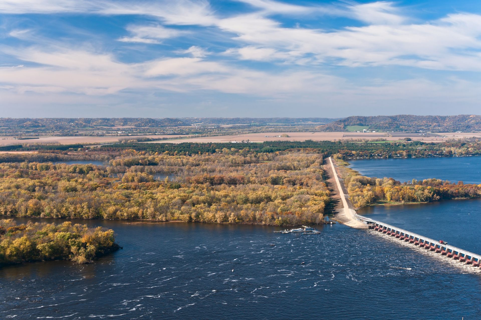 Aerial view: Bridge over dark water, forested islands with autumn colors, under a blue sky with clouds.