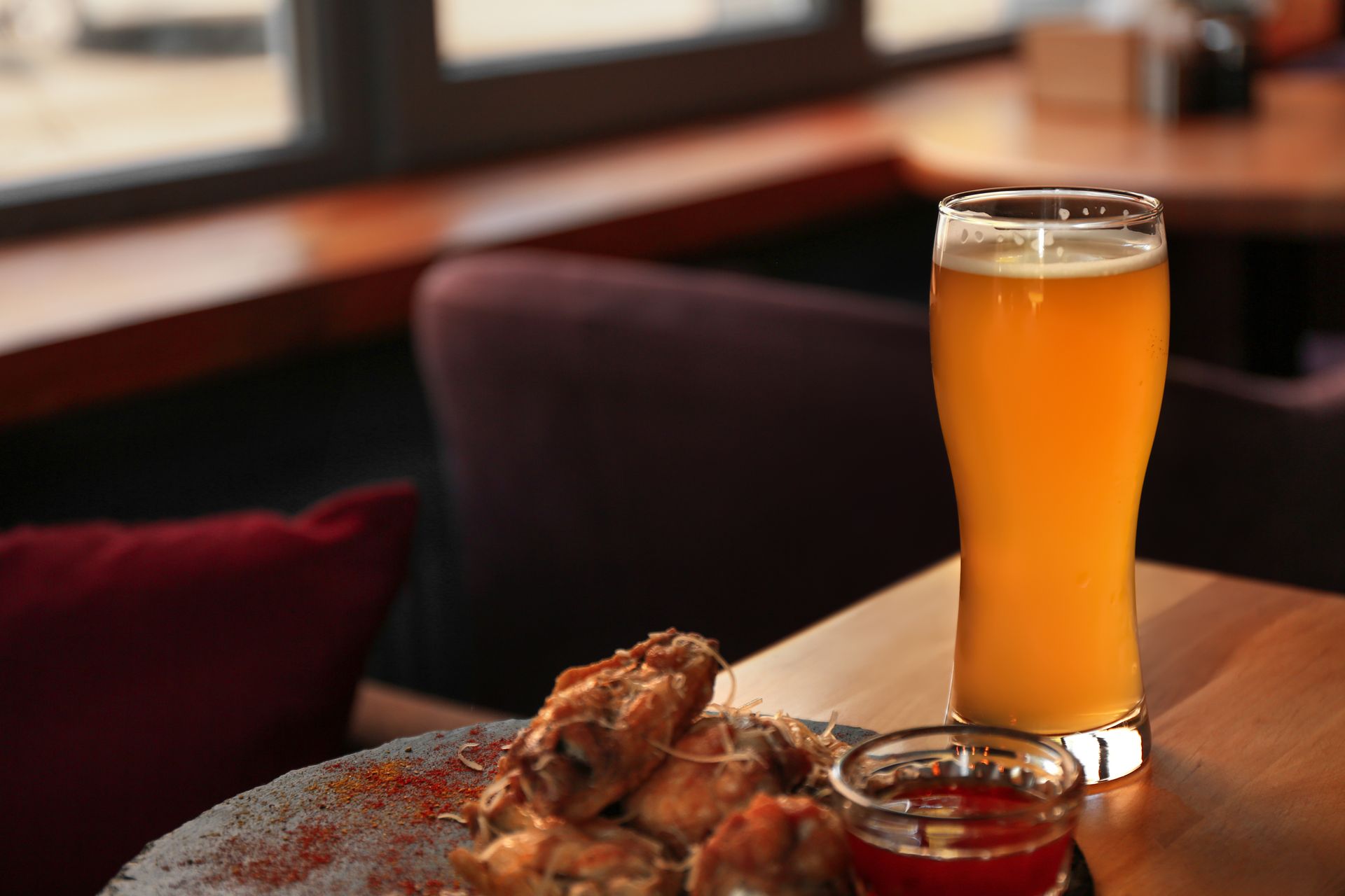 Beer glass and plate of chicken wings with dipping sauce on a table in a restaurant.