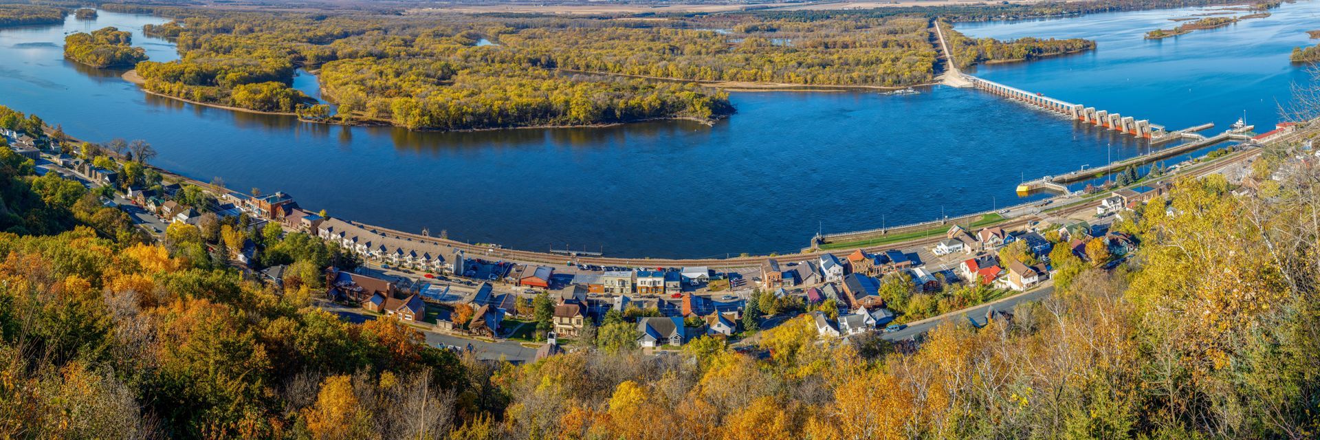 A scenic view of a river, with a town and islands, surrounded by autumn trees.
