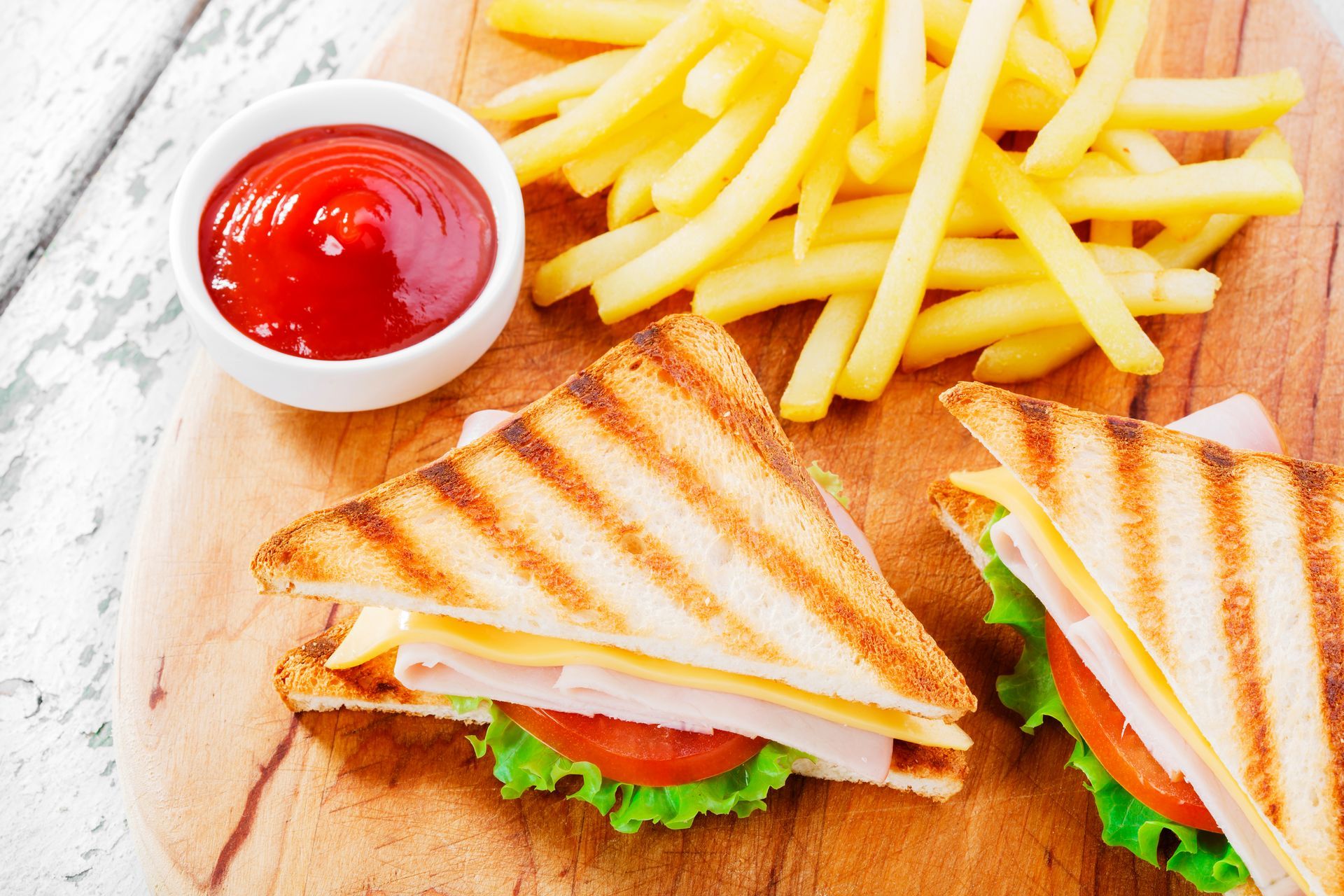 Grilled sandwiches, fries, and ketchup on a wooden board.
