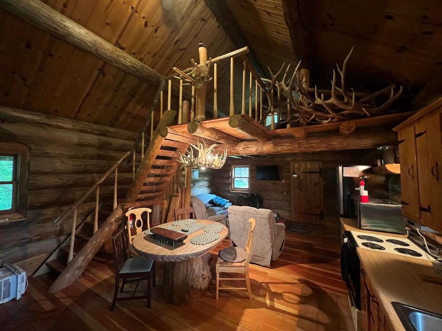 Cozy cabin interior with wood paneling, kitchen, living area, and a dining table.