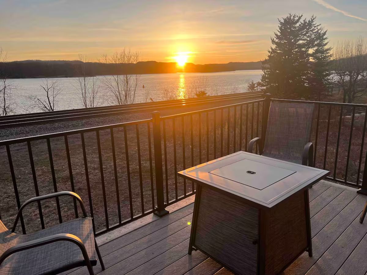 Deck with table and chairs overlooking a lake at sunset.