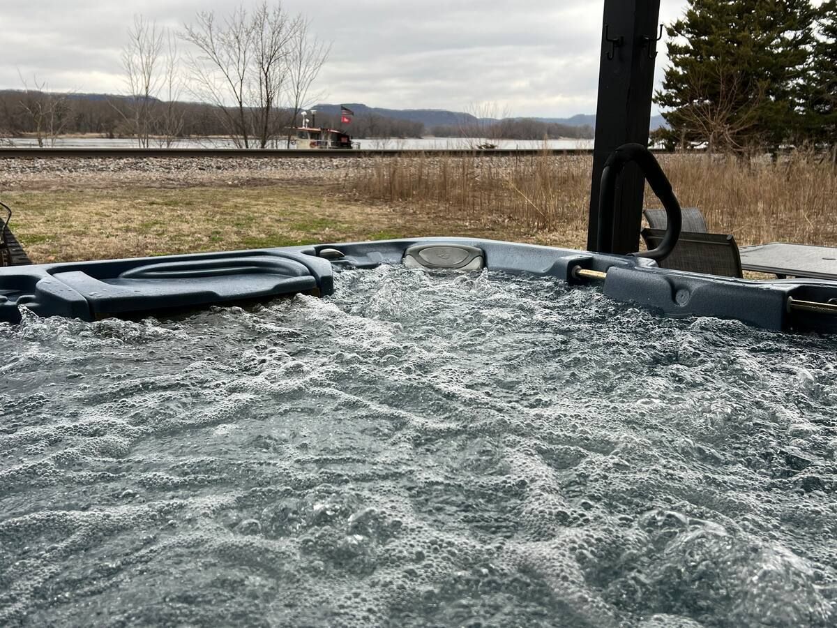 Bubbling hot tub outdoors with a train passing in the background on a cloudy day.