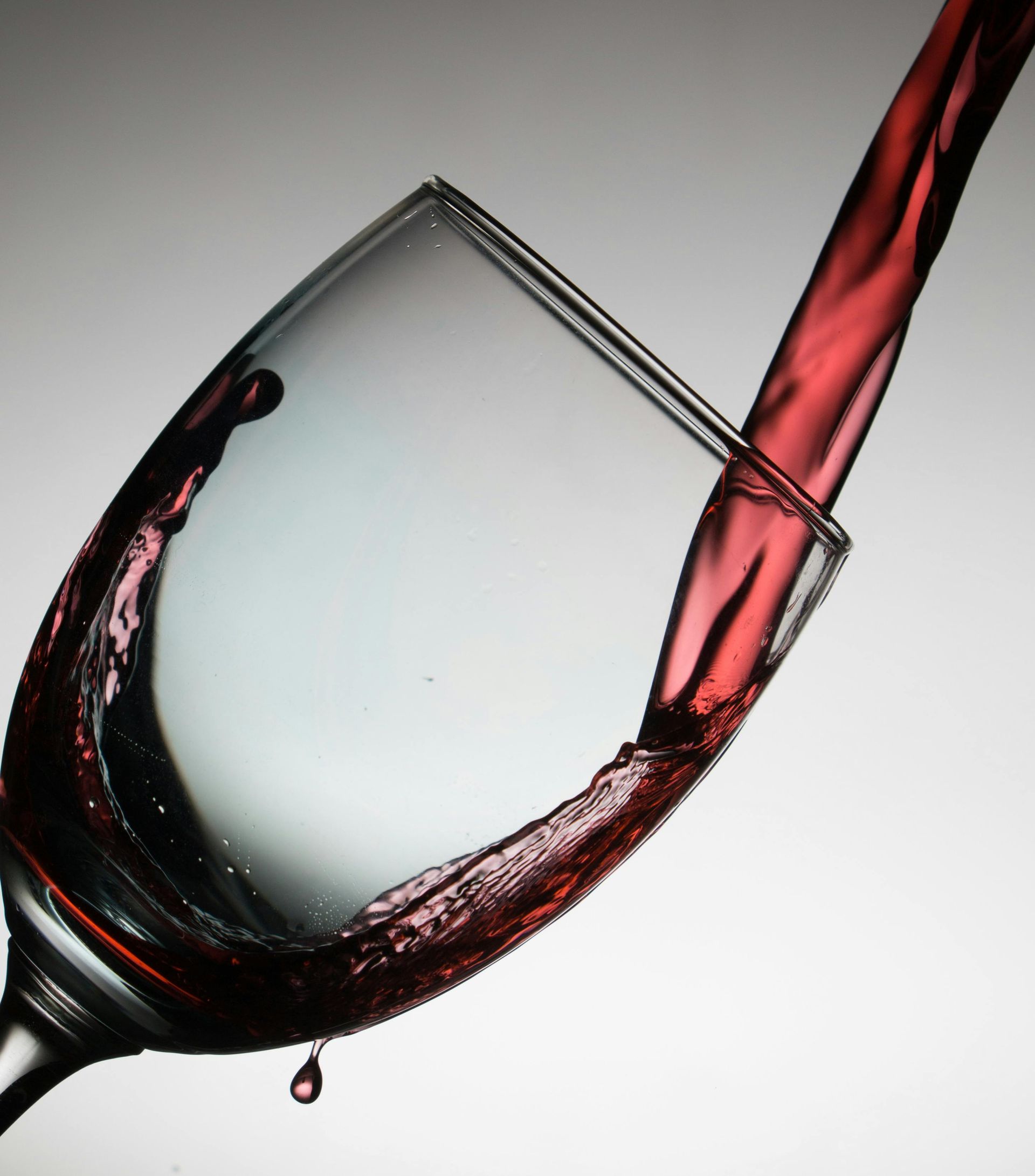 Red wine being poured into a glass against a white background.