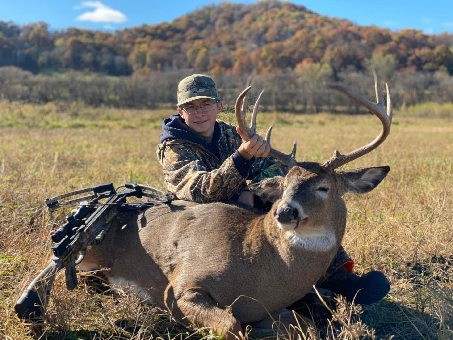 A person in camouflage holds a large buck with impressive antlers in a field.