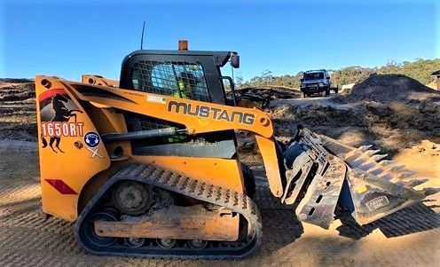 A yellow mustang bulldozer is parked on a dirt road.