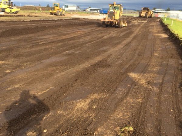 A group of construction vehicles are working on a dirt road.
