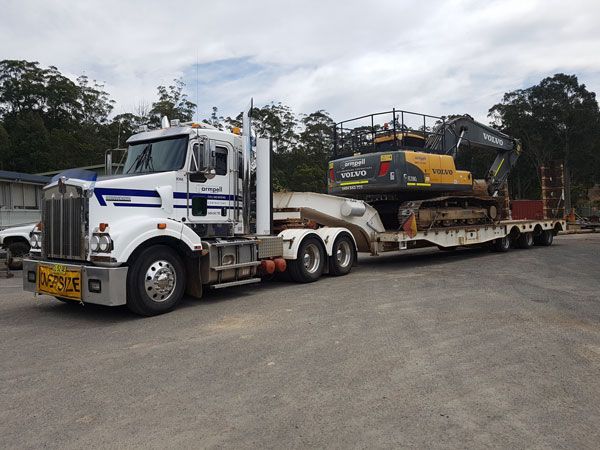 A semi truck is carrying a large excavator on a trailer.