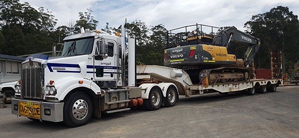 A semi truck is carrying a large excavator on a trailer.