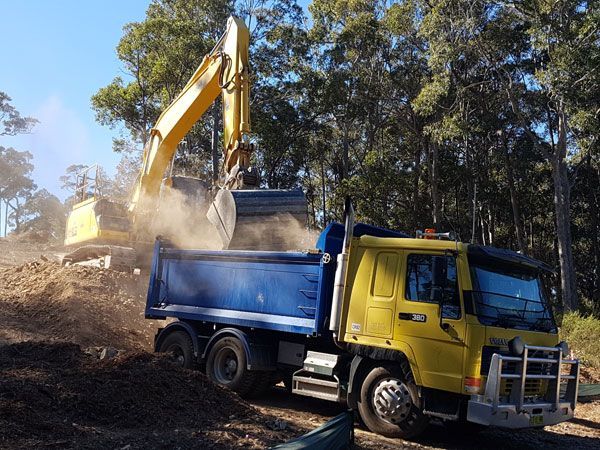 A yellow dump truck is being loaded with dirt by an excavator.