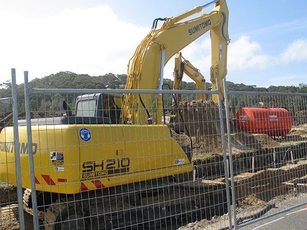 A yellow excavator is parked behind a fence at a construction site