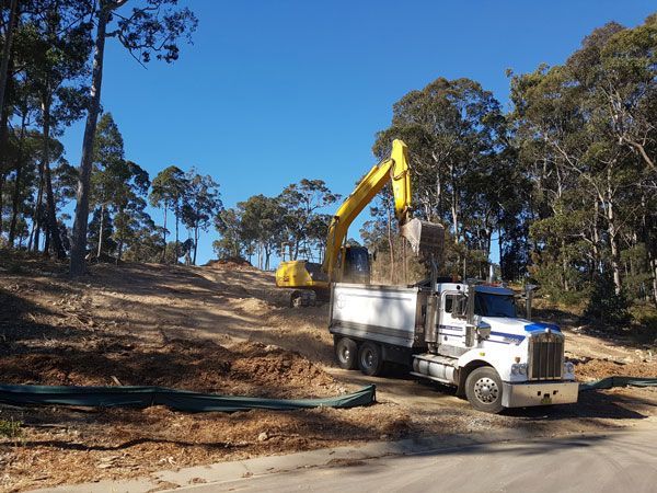 A white truck is driving down a dirt road next to a yellow excavator.