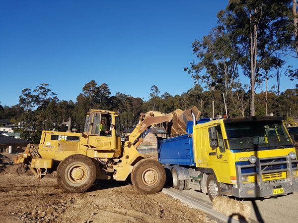 A dump truck is being towed by a bulldozer on a dirt road
