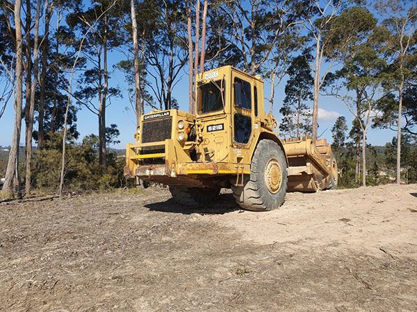 A large yellow truck is parked in a dirt field with trees in the background.