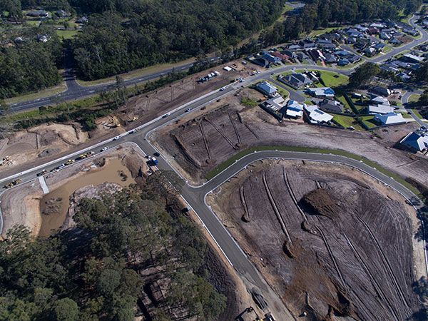 An aerial view of a construction site with a road and houses in the background.