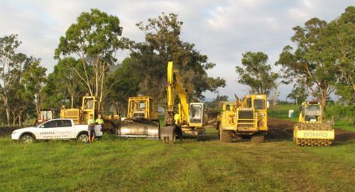 A group of construction vehicles are parked in a grassy field.