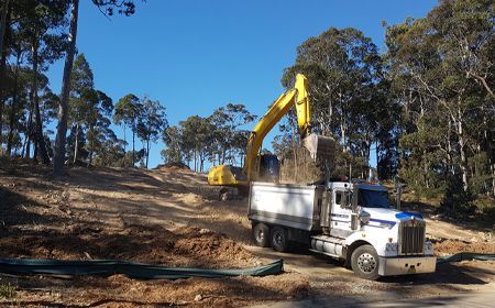 A dump truck is being loaded with dirt by an excavator.